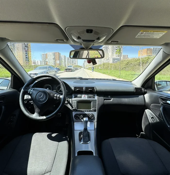 Interior of Mercedes C-Class 2007 with dark seats, steering wheel and automatic gear selector viewed from the rear seats