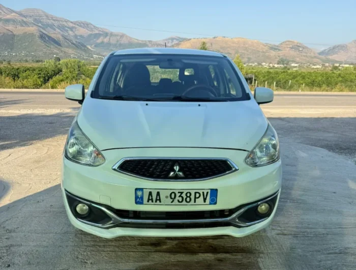 White Mitsubishi Space Star 2017 1.0 petrol manual five‑door hatchback parked near Albanian mountains and Tirana Airport, available for car rental with TiRental