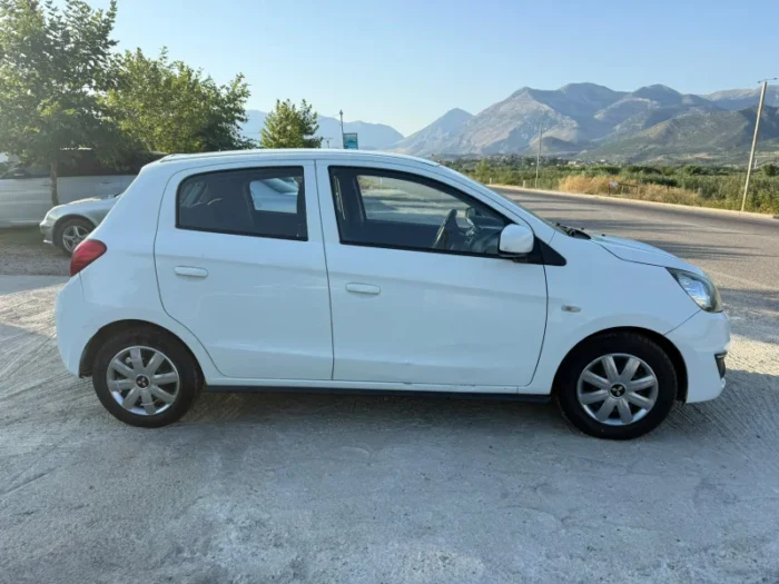 White Mitsubishi Space Star 2017 1.0 petrol manual five‑door hatchback parked near Albanian mountains and Tirana Airport, available for car rental with TiRental