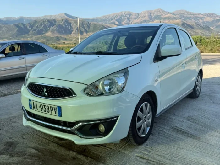 White Mitsubishi Space Star 2017 1.0 petrol manual five‑door hatchback parked near Albanian mountains and Tirana Airport, available for car rental with TiRental