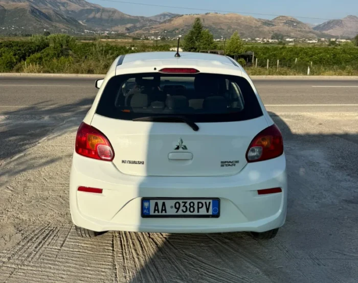 White Mitsubishi Space Star 2017 1.0 petrol manual five‑door hatchback parked near Albanian mountains and Tirana Airport, available for car rental with TiRental